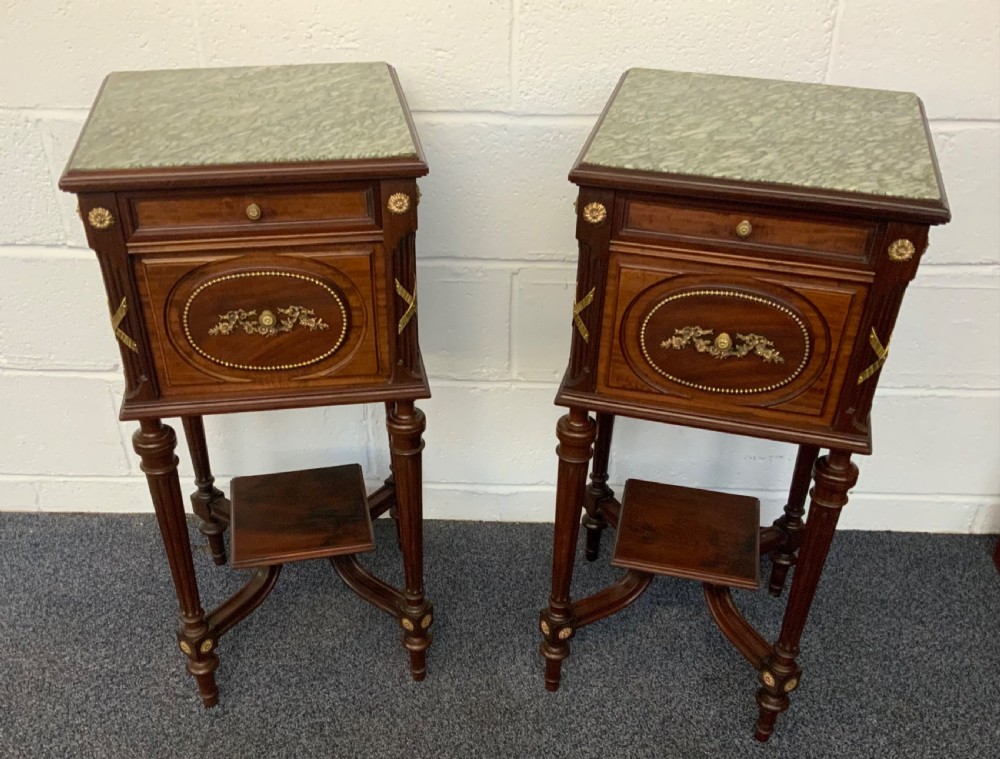 A matching pair of tall French Neoclassical mahogany bedside cabinets featuring green marble tops, gilt brass mounts, and slender turned legs.
