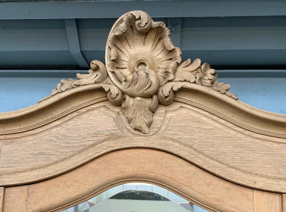 A large triple-door bleached oak French armoire featuring arched mirror panels, carved rococo cresting, bottom drawers, and cabriole feet. View II