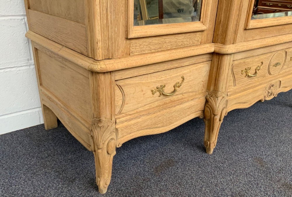 A large triple-door bleached oak French armoire featuring arched mirror panels, carved rococo cresting, bottom drawers, and cabriole feet. View VI
