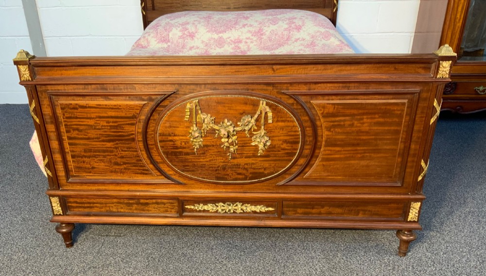 A French Neoclassical king-size wooden bedstead featuring detailed brass swags, ribbon cresting, finials, and an oval medallion motif on the footboard. View II