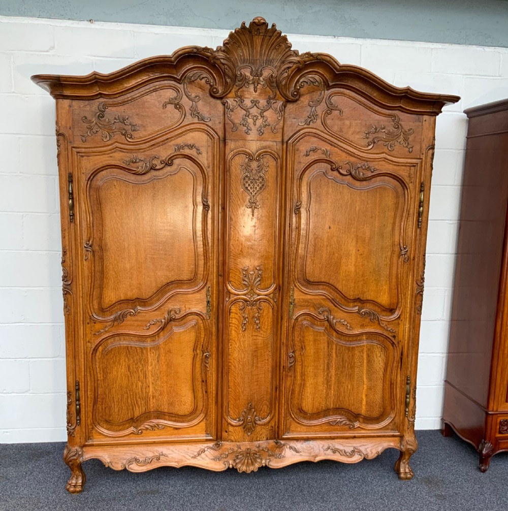 A large French Provincial carved oak armoire featuring double panelled doors, intricate cresting, brass hardware, and cabriole feet.