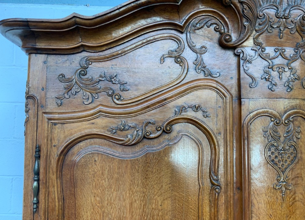 A large French Provincial carved oak armoire featuring double panelled doors, intricate cresting, brass hardware, and cabriole feet. View IV
