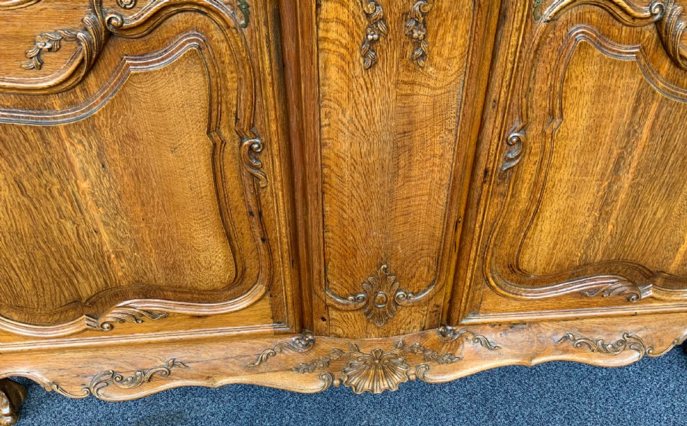 A large French Provincial carved oak armoire featuring double panelled doors, intricate cresting, brass hardware, and cabriole feet. View VI