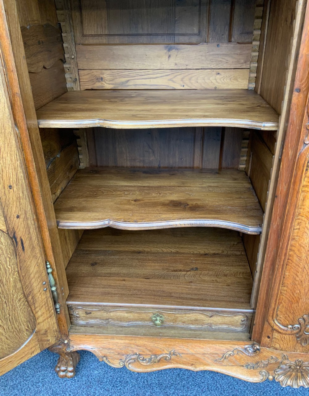 A large French Provincial carved oak armoire featuring double panelled doors, intricate cresting, brass hardware, and cabriole feet. View XIII