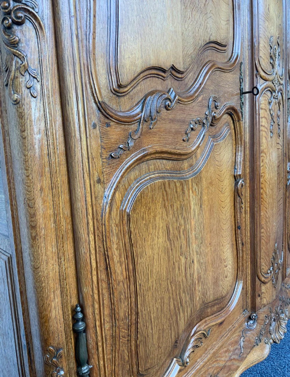 A large French Provincial carved oak armoire featuring double panelled doors, intricate cresting, brass hardware, and cabriole feet. View XVII