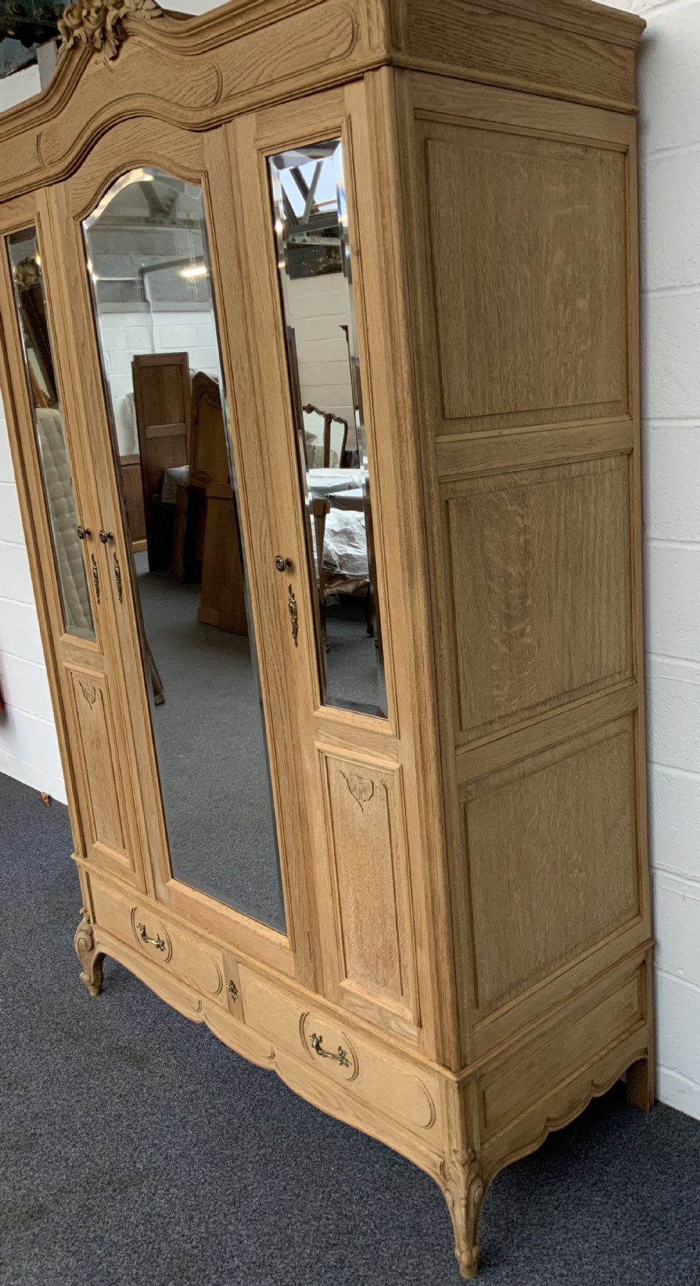 A large bleached oak triple-door armoire featuring glass mirror panels, a carved top crest pediment, base drawers, and carved cabriole feet. View IV