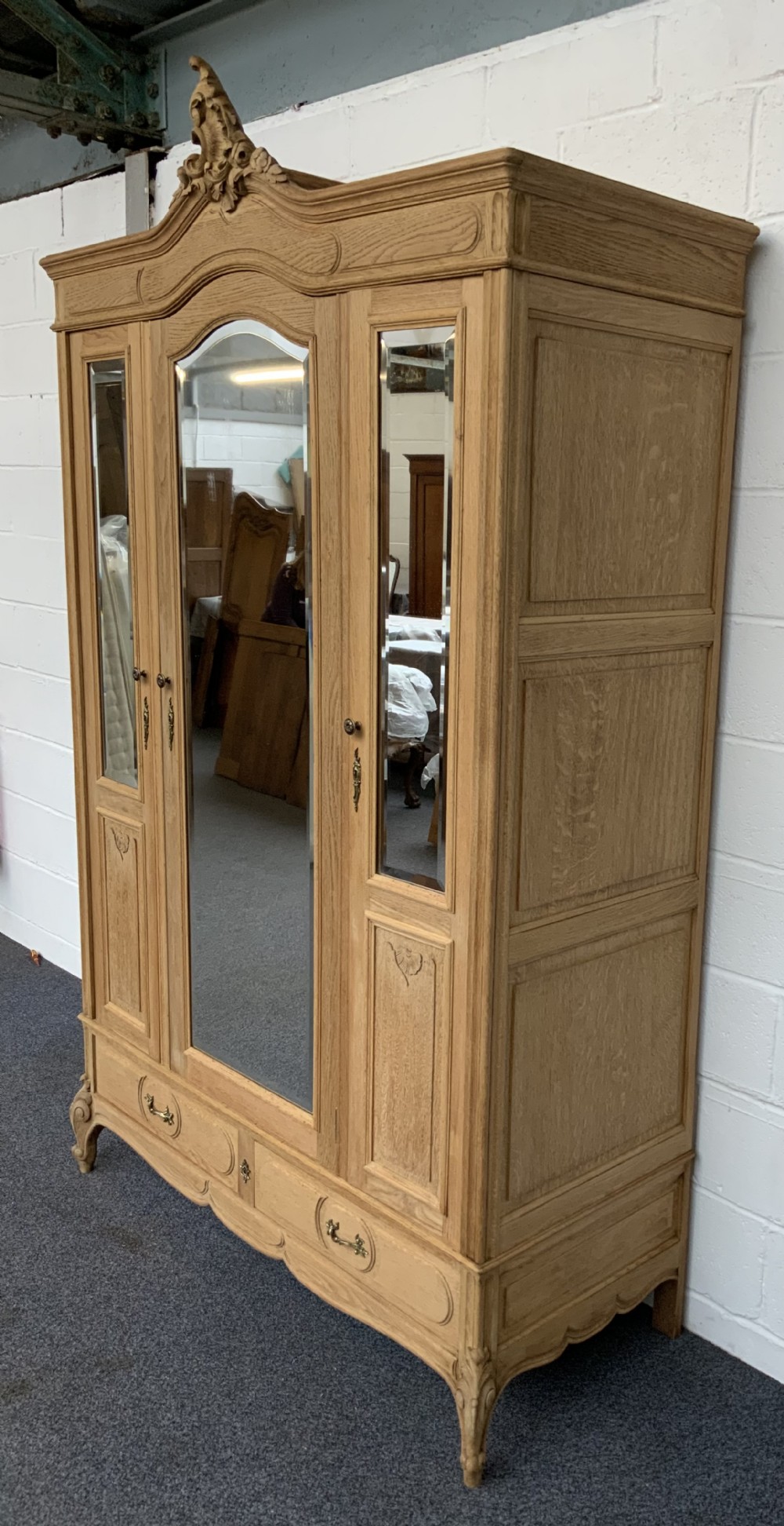 A large bleached oak triple-door armoire featuring glass mirror panels, a carved top crest pediment, base drawers, and carved cabriole feet. View V
