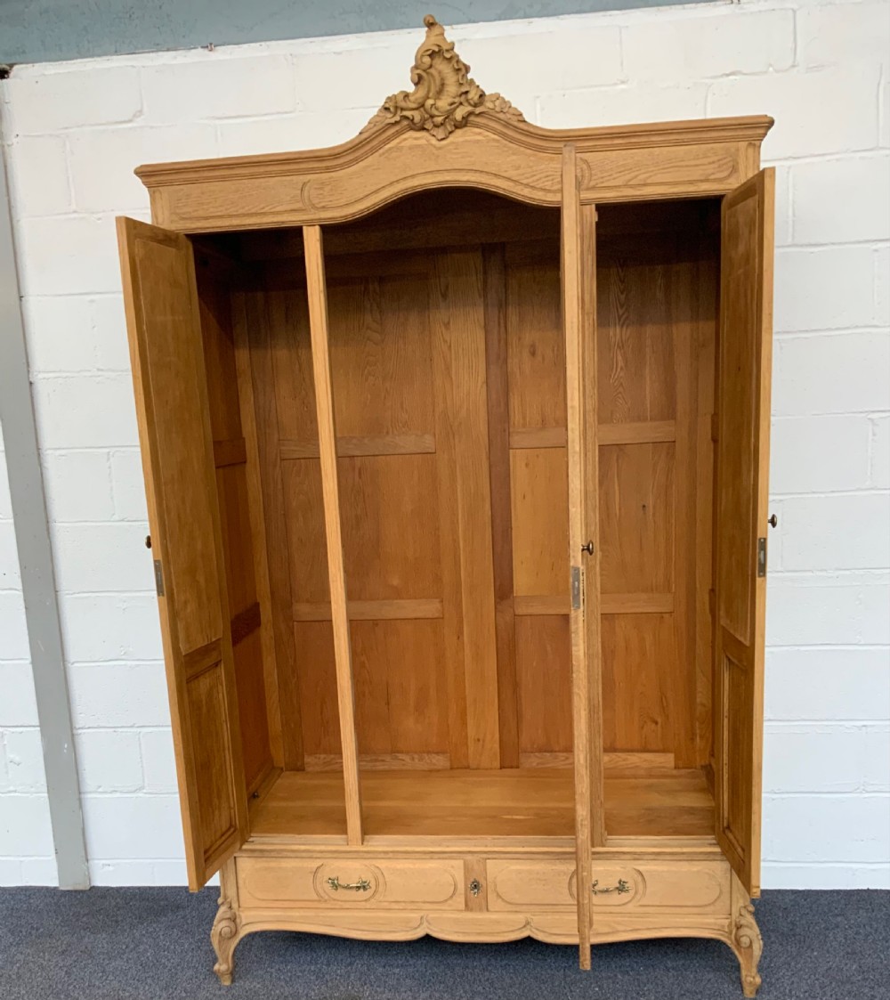 A large bleached oak triple-door armoire featuring glass mirror panels, a carved top crest pediment, base drawers, and carved cabriole feet. View IX