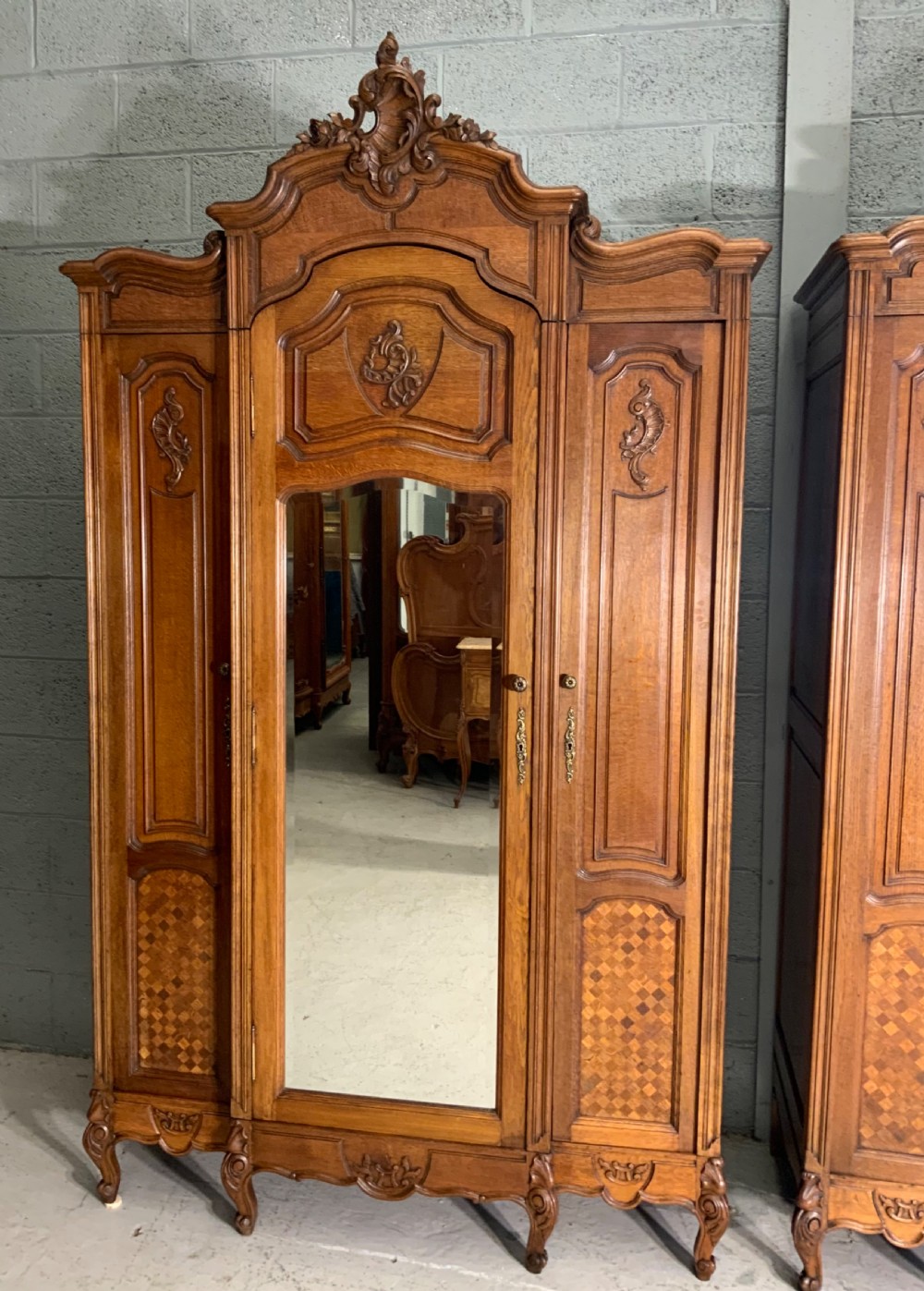 A pair of carved oak French provincial armoires featuring arched mirrored doors, parquetry lower panels, and elaborate carved crests. View II