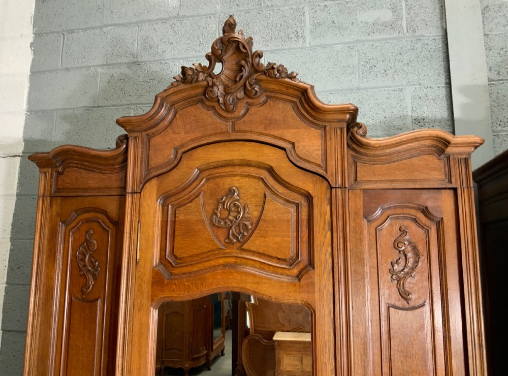 A pair of carved oak French provincial armoires featuring arched mirrored doors, parquetry lower panels, and elaborate carved crests. View III