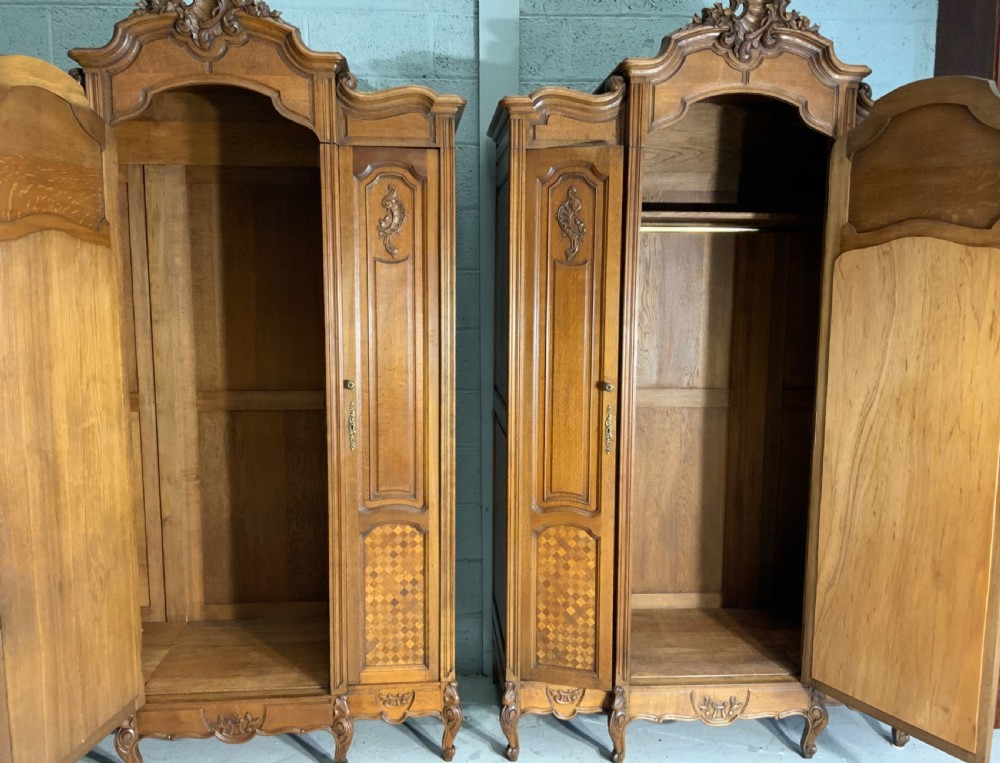A pair of carved oak French provincial armoires featuring arched mirrored doors, parquetry lower panels, and elaborate carved crests. View IV