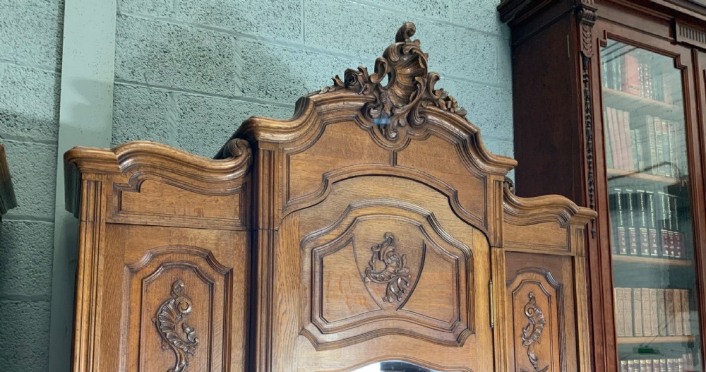A pair of carved oak French provincial armoires featuring arched mirrored doors, parquetry lower panels, and elaborate carved crests. View V