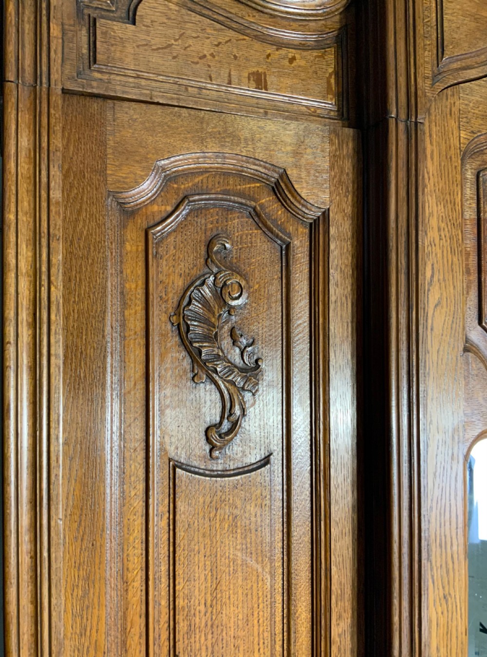 A pair of carved oak French provincial armoires featuring arched mirrored doors, parquetry lower panels, and elaborate carved crests. View VI