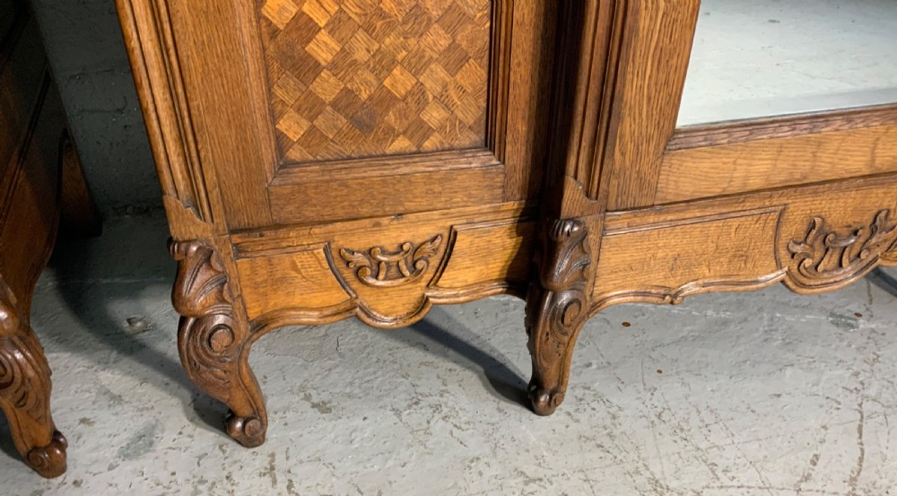 A pair of carved oak French provincial armoires featuring arched mirrored doors, parquetry lower panels, and elaborate carved crests. View VII