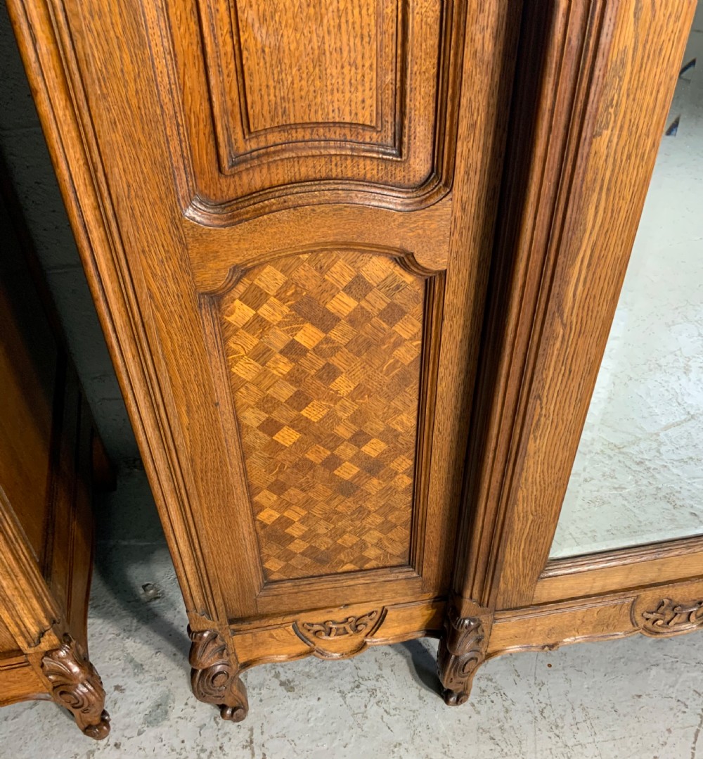 A pair of carved oak French provincial armoires featuring arched mirrored doors, parquetry lower panels, and elaborate carved crests. View VIII