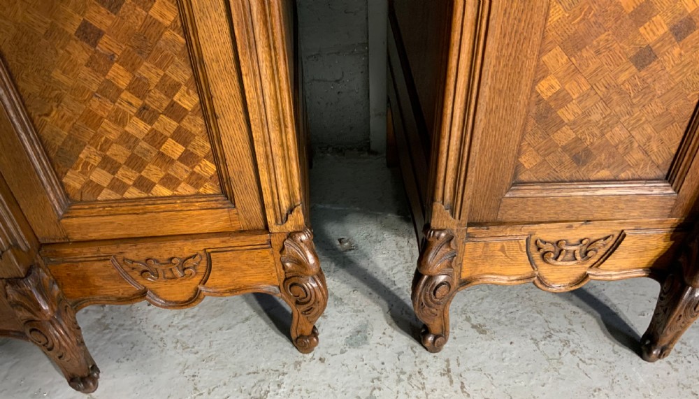 A pair of carved oak French provincial armoires featuring arched mirrored doors, parquetry lower panels, and elaborate carved crests. View IX