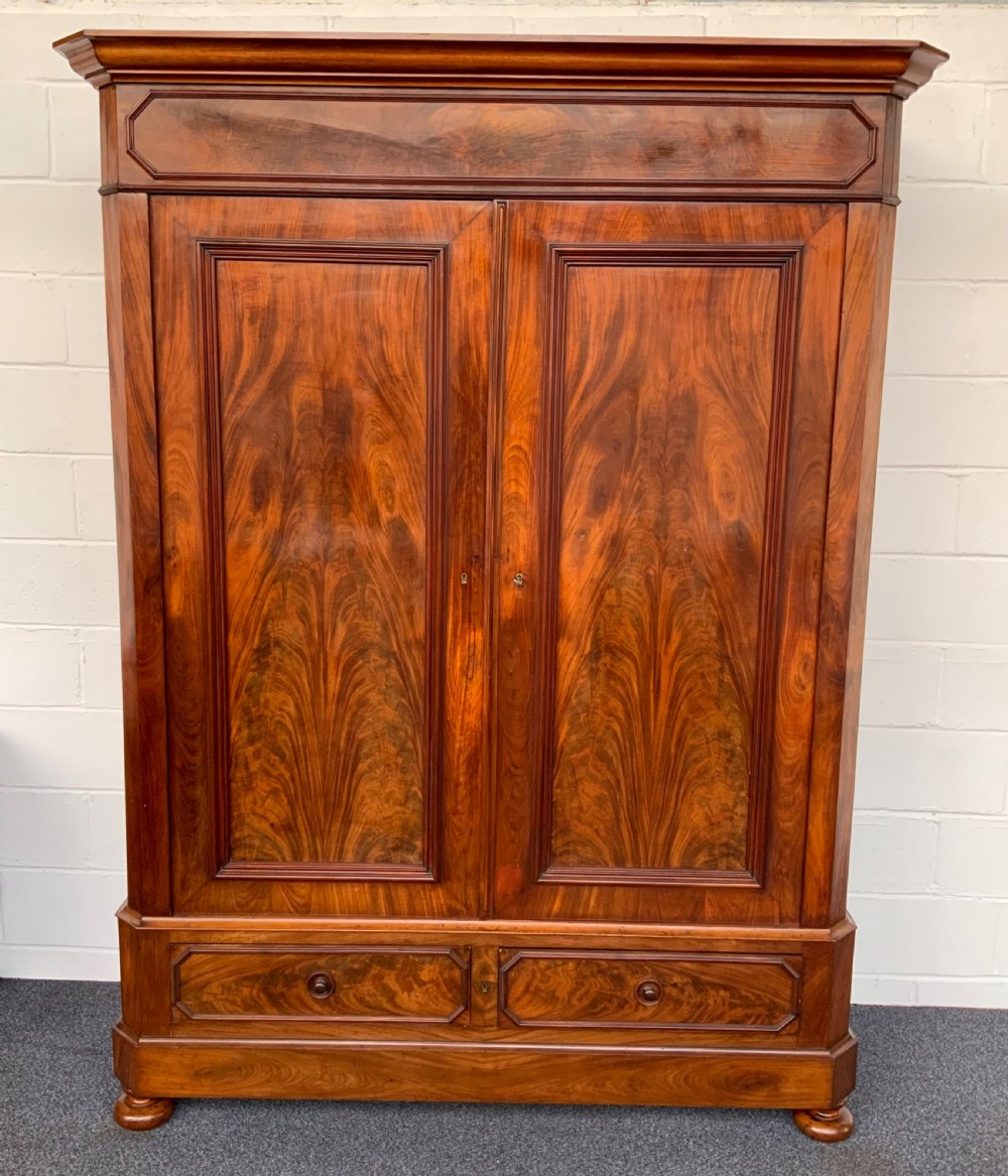 A 19th-century French mahogany armoire with flame-veneered double doors, a top moulding, two base drawers, and turned bun feet.