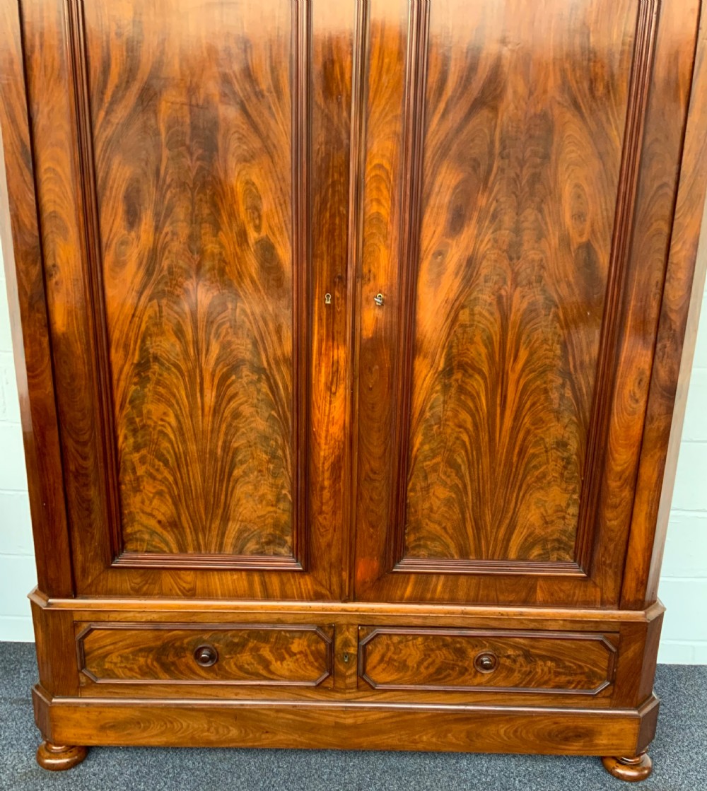 A 19th-century French mahogany armoire with flame-veneered double doors, a top moulding, two base drawers, and turned bun feet. View II