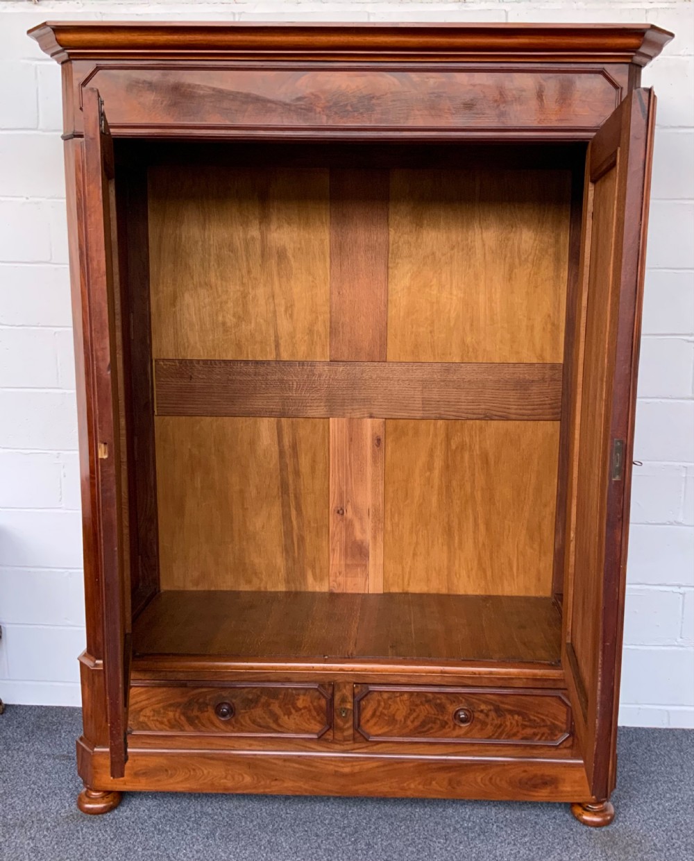 A 19th-century French mahogany armoire with flame-veneered double doors, a top moulding, two base drawers, and turned bun feet. View V