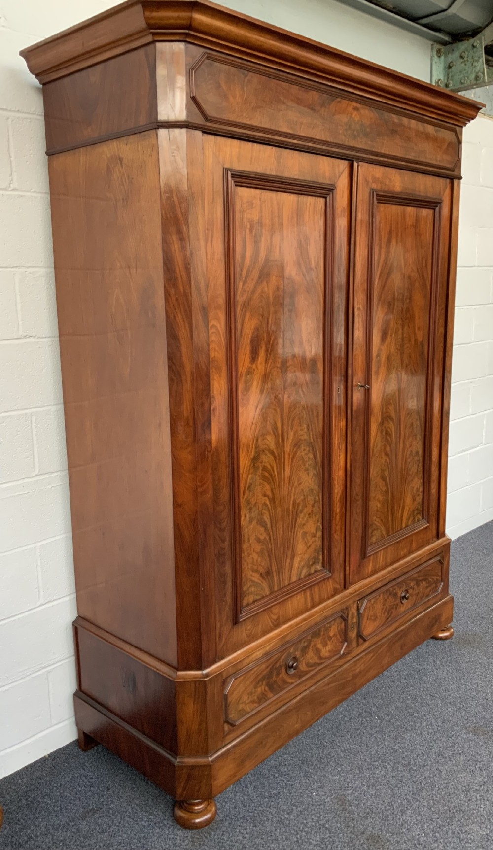 A 19th-century French mahogany armoire with flame-veneered double doors, a top moulding, two base drawers, and turned bun feet. View X