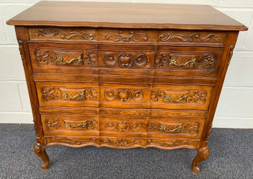 A French Provincial carved oak chest of drawers featuring three serpentine-front drawers, relief floral carvings, and ornate brass handles. View VII