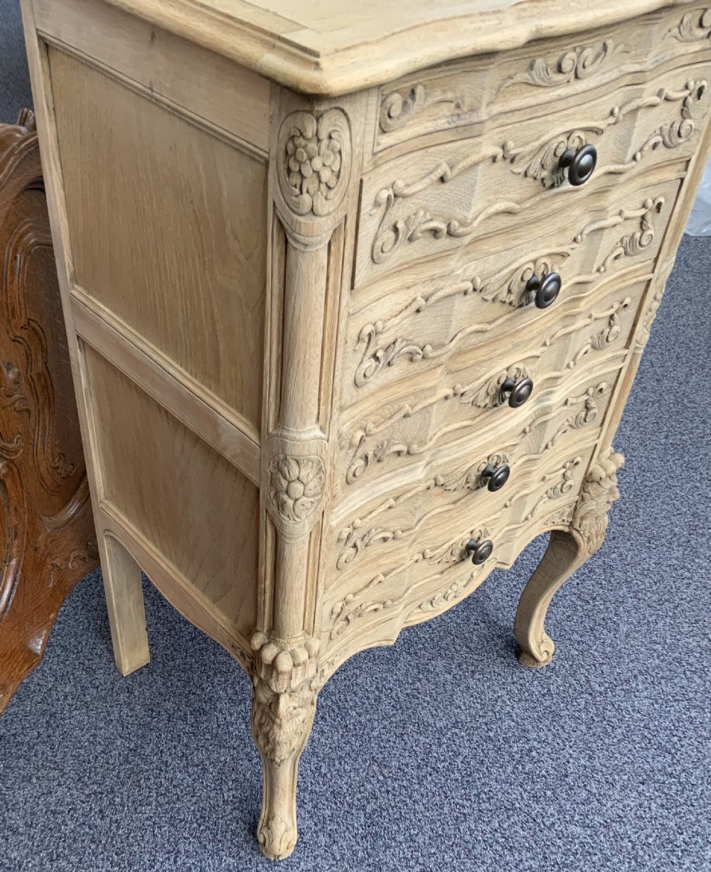 A narrow bleached oak French chest featuring five carved drawers with metal knobs, resting on curved cabriole legs. View IV