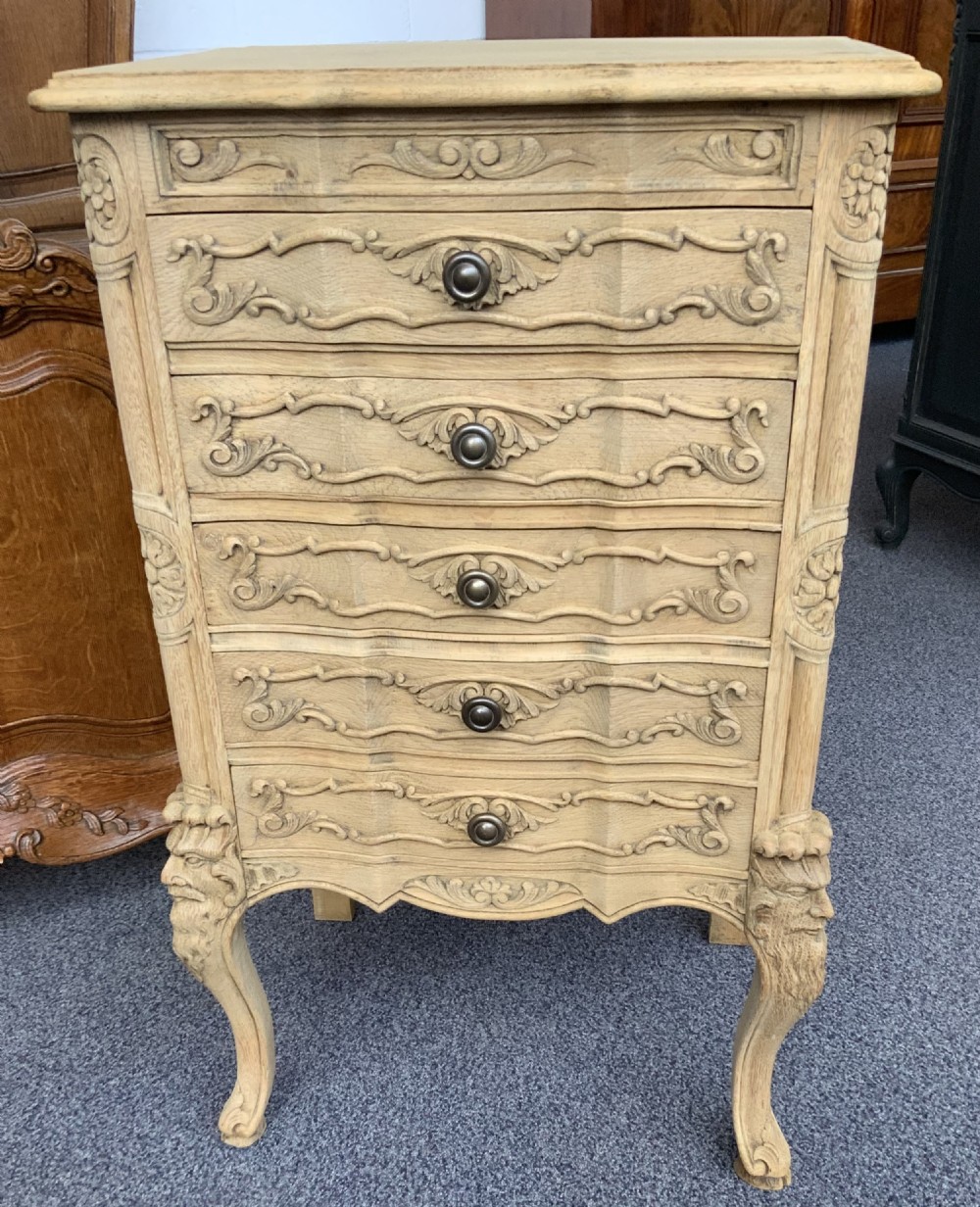 A narrow bleached oak French chest featuring five carved drawers with metal knobs, resting on curved cabriole legs. View VI