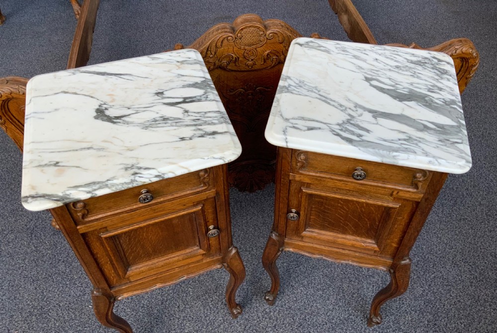 A pair of French oak bedside cabinets featuring white marble tops, single drawers, panelled doors, and carved cabriole legs. View II