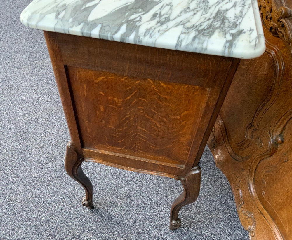A pair of French oak bedside cabinets featuring white marble tops, single drawers, panelled doors, and carved cabriole legs. View IV
