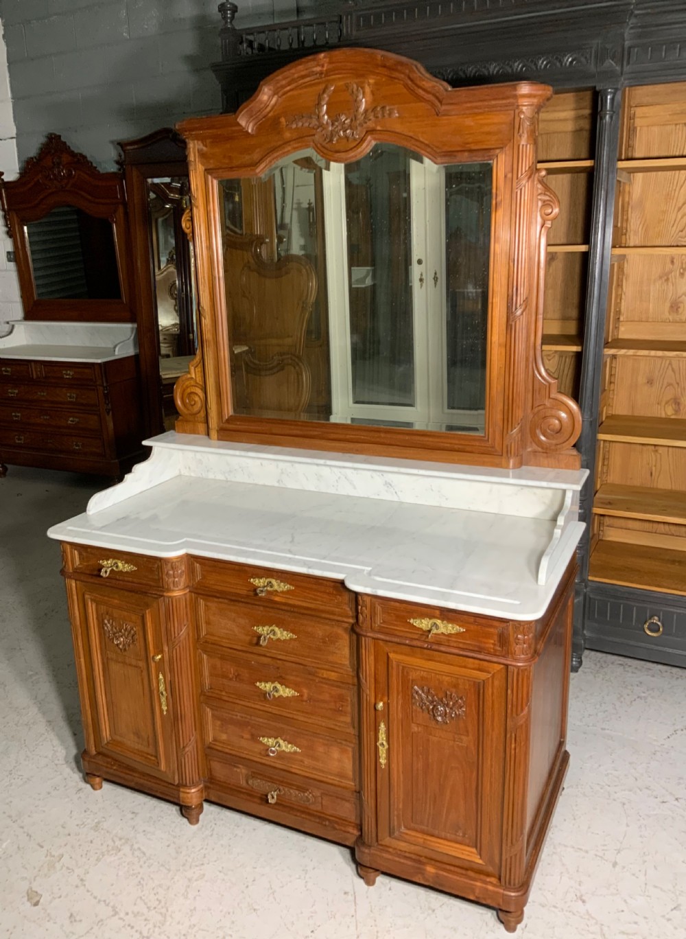 An antique mahogany French washstand featuring a white marble top, integrated arched mirror, multiple drawers, and side cupboards with brass handles.