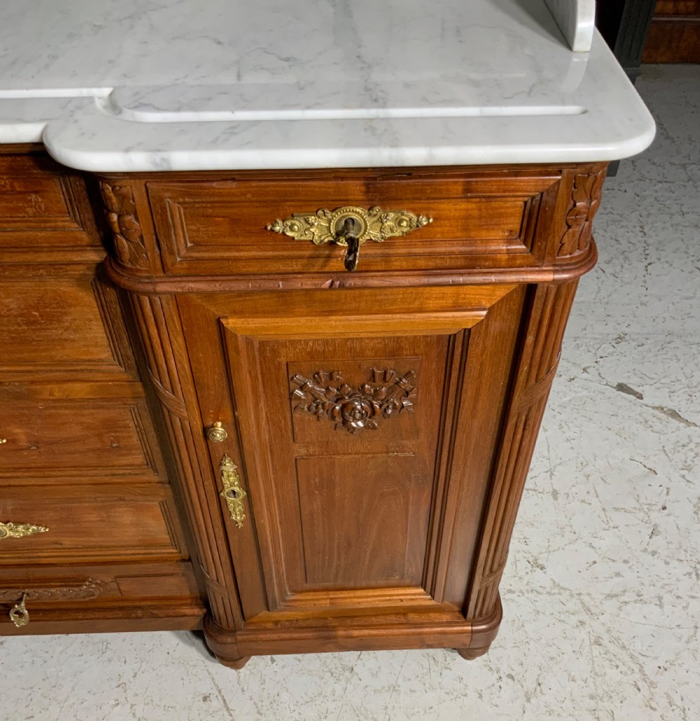 An antique mahogany French washstand featuring a white marble top, integrated arched mirror, multiple drawers, and side cupboards with brass handles. View XIII