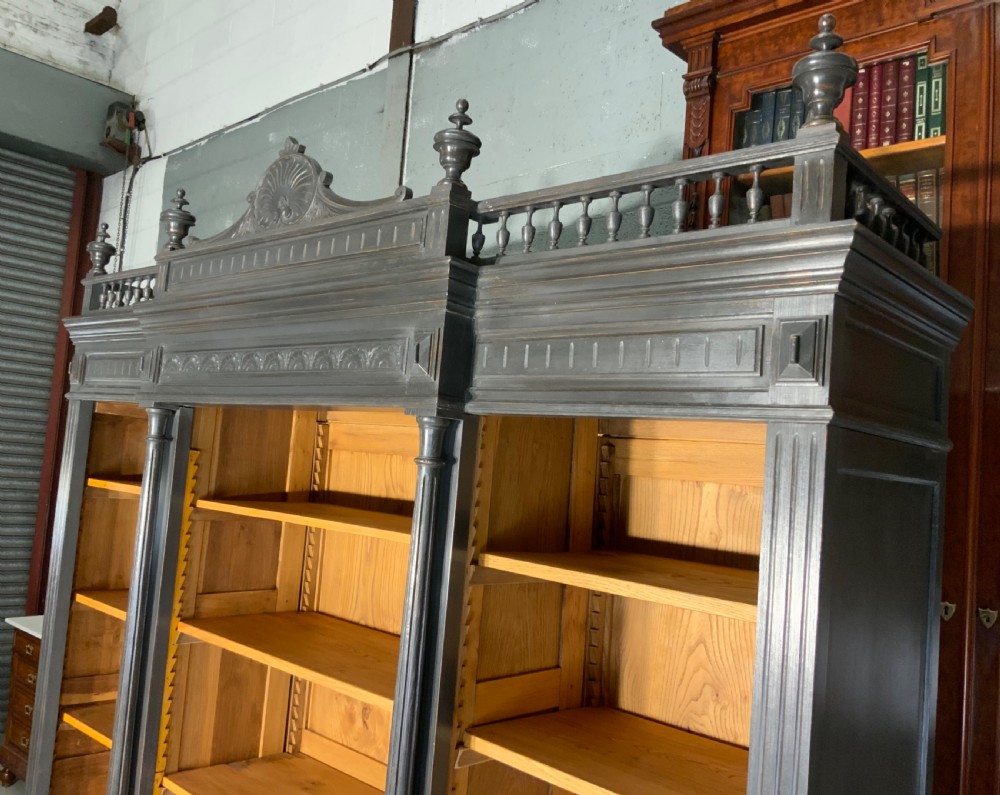 A large antique French open bookcase featuring a dark painted frame with carved shell cresting and finials, contrasting natural pine shelving, and three bottom drawers with brass handles. View IV