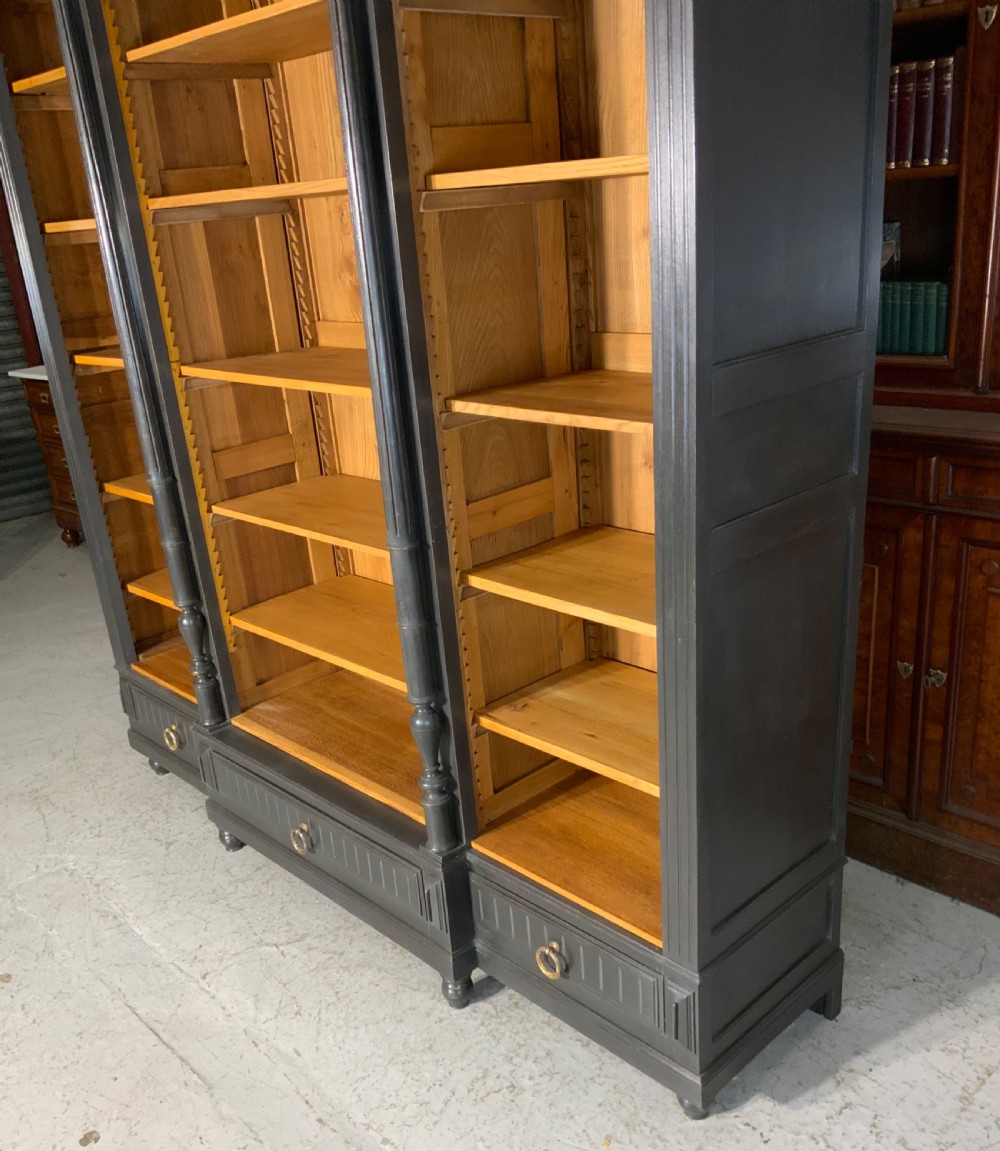 A large antique French open bookcase featuring a dark painted frame with carved shell cresting and finials, contrasting natural pine shelving, and three bottom drawers with brass handles. View VI