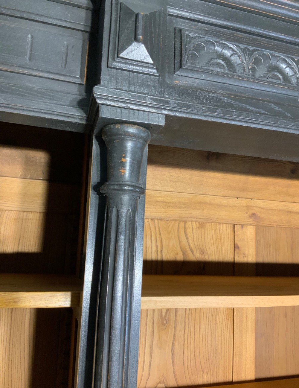 A large antique French open bookcase featuring a dark painted frame with carved shell cresting and finials, contrasting natural pine shelving, and three bottom drawers with brass handles. View XI