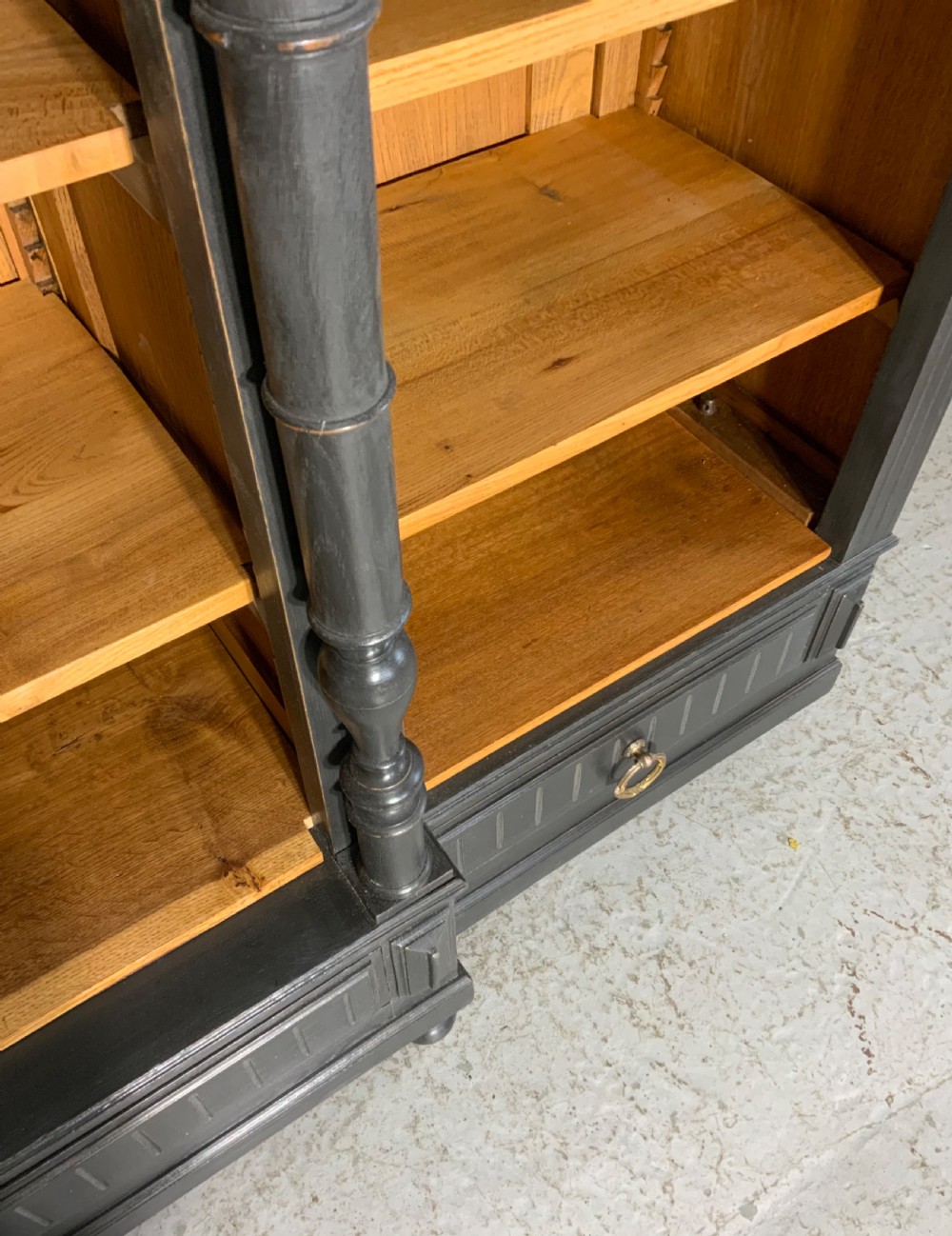 A large antique French open bookcase featuring a dark painted frame with carved shell cresting and finials, contrasting natural pine shelving, and three bottom drawers with brass handles. View XIII