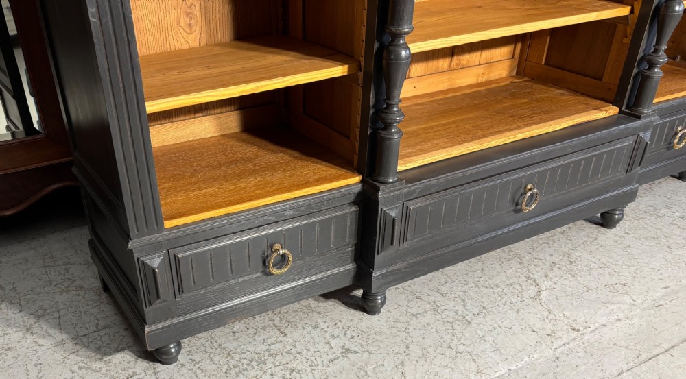 A large antique French open bookcase featuring a dark painted frame with carved shell cresting and finials, contrasting natural pine shelving, and three bottom drawers with brass handles. View XVII