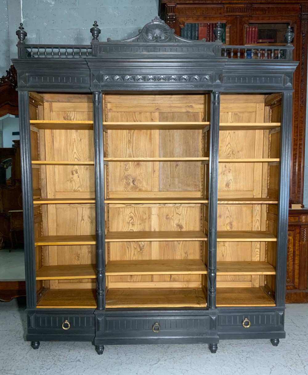 A large antique French open bookcase featuring a dark painted frame with carved shell cresting and finials, contrasting natural pine shelving, and three bottom drawers with brass handles. View XIX