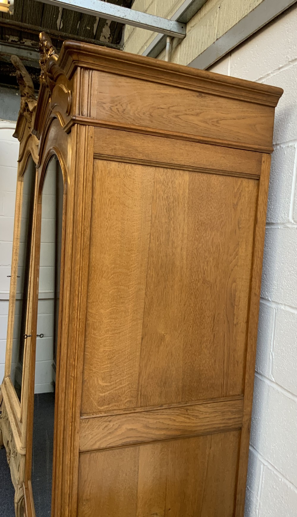 A tall French oak single-door armoire featuring an arched mirrored door, a carved cresting pediment, a bottom drawer, and cabriole feet. View III
