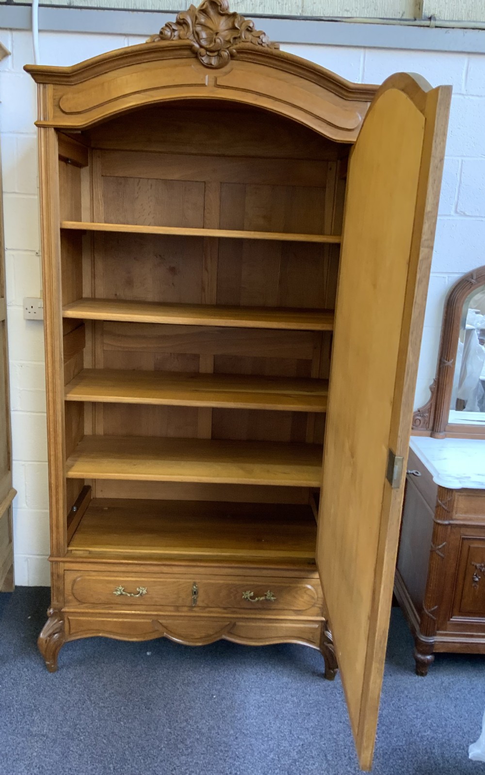 A tall French oak single-door armoire featuring an arched mirrored door, a carved cresting pediment, a bottom drawer, and cabriole feet. View V