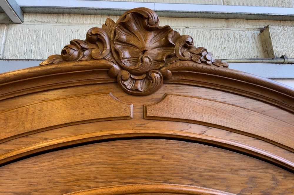 A tall French oak single-door armoire featuring an arched mirrored door, a carved cresting pediment, a bottom drawer, and cabriole feet. View VI