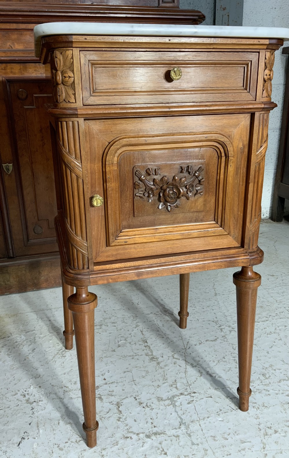 A pair of French Louis XVI style walnut bedside cabinets with grey-veined white marble tops, carved door panels, and turned legs. View IV