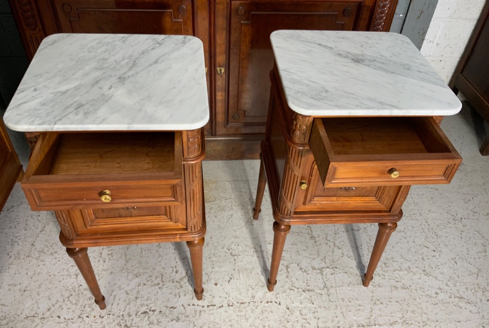 A pair of French Louis XVI style walnut bedside cabinets with grey-veined white marble tops, carved door panels, and turned legs. View VII
