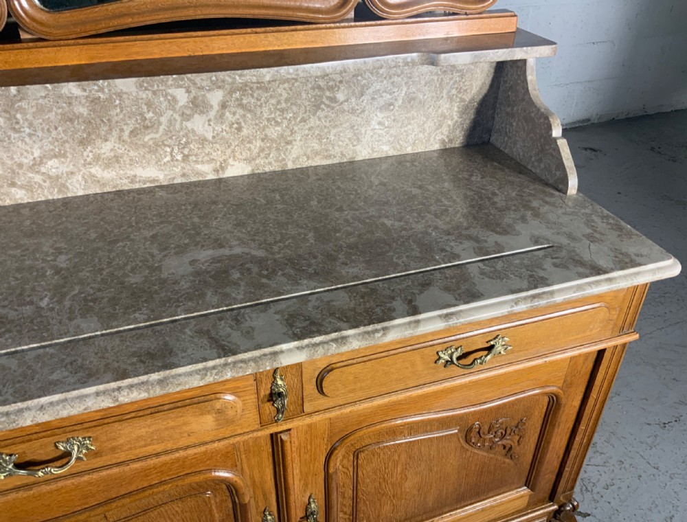 A carved oak French dressing table featuring a marbled stone top, a matching splashback shelf, an attached three-panel triptych mirror, and two drawers above a two-door cabinet. View V