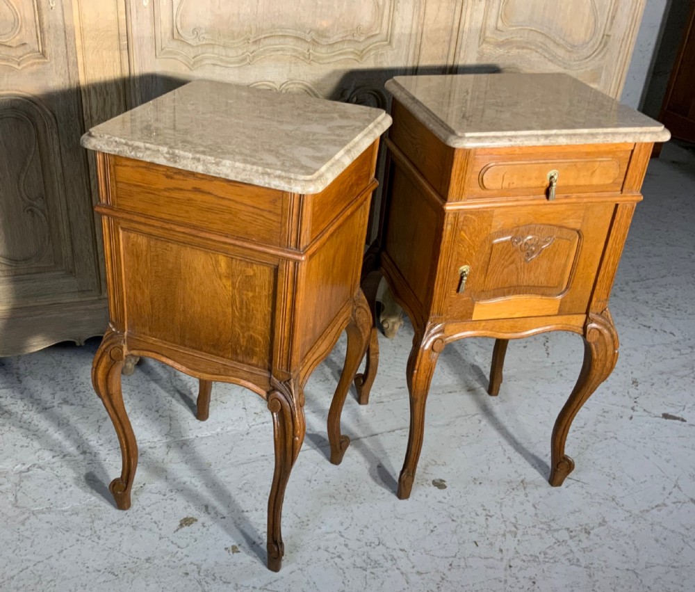 A matching pair of French oak bedside cabinets featuring inset beige marble tops, single frieze drawers, carved cupboard doors, and slender cabriole legs. View III