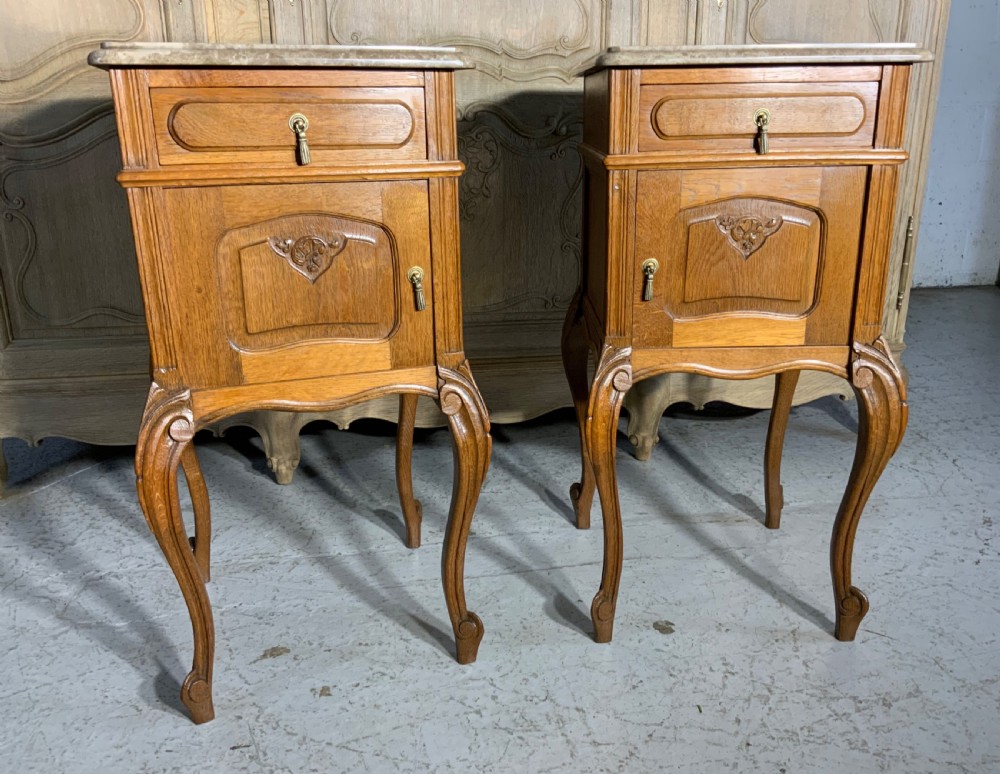 A matching pair of French oak bedside cabinets featuring inset beige marble tops, single frieze drawers, carved cupboard doors, and slender cabriole legs. View VIII