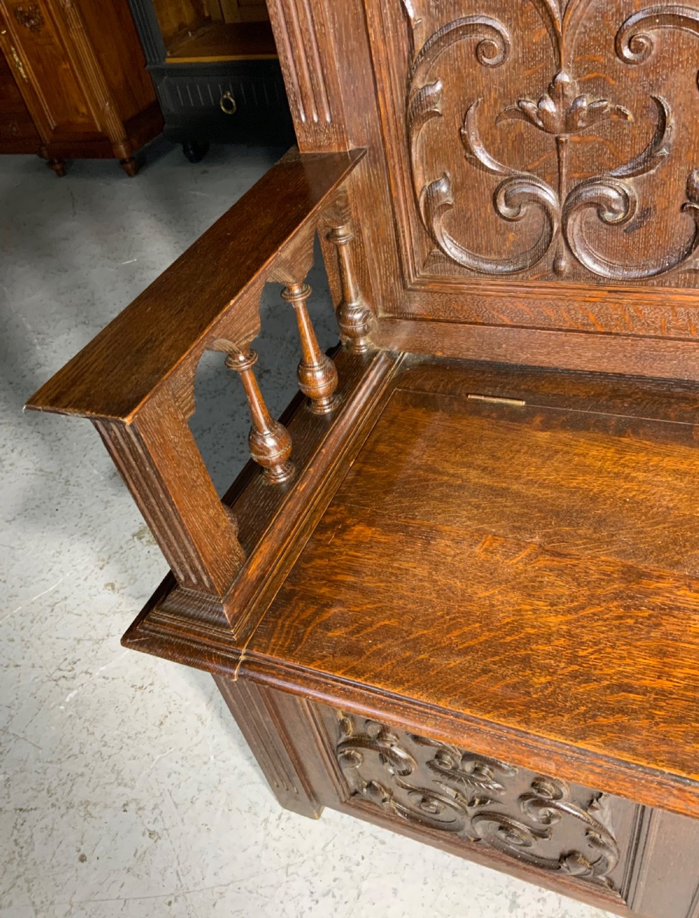 A carved dark oak French hall seat featuring a high backrest with scrollwork relief panels, turned arm spindles, and a hinged storage seat base. View VIII