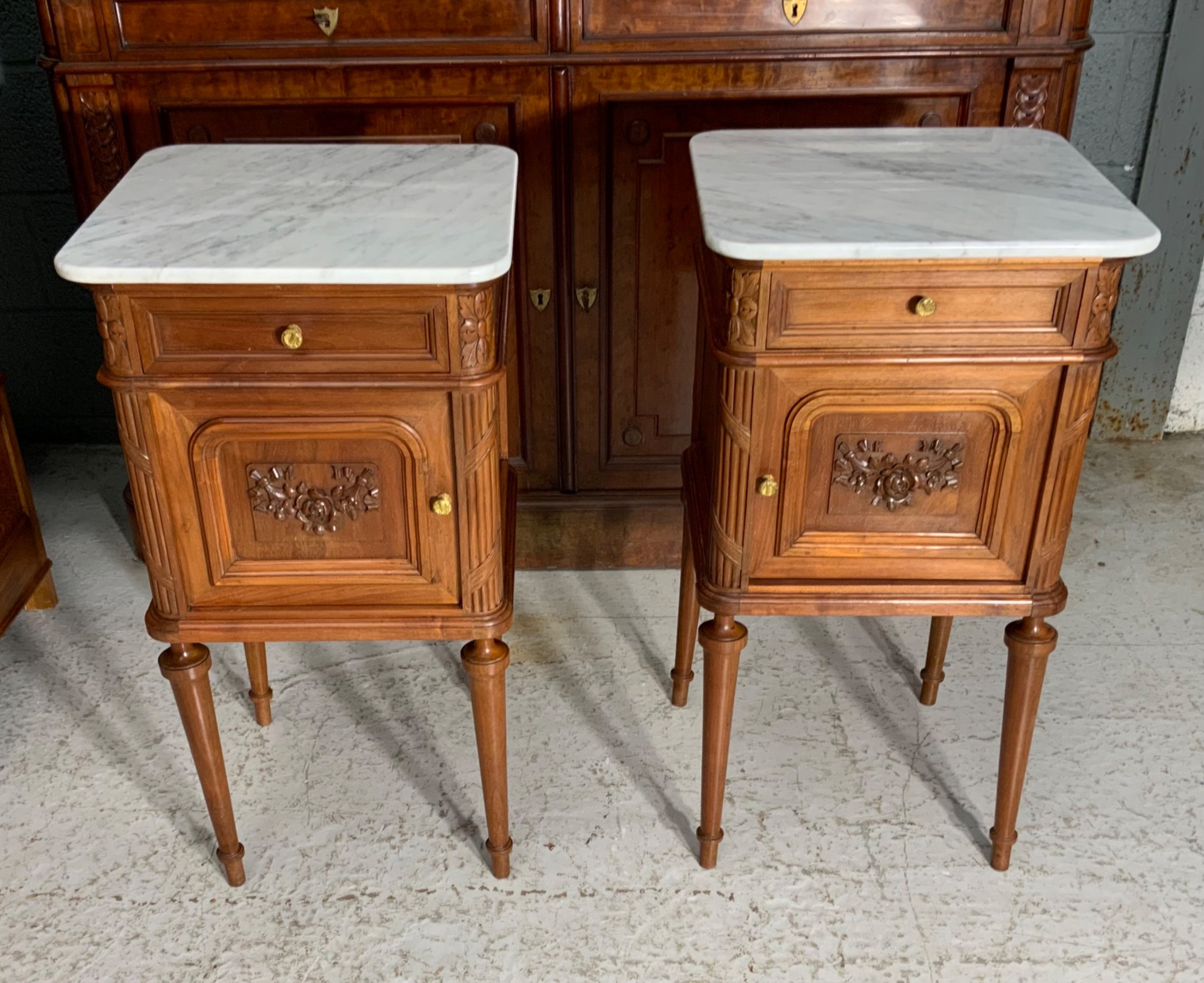 A pair of French Louis XVI style walnut bedside cabinets with grey-veined white marble tops, carved door panels, and turned legs.