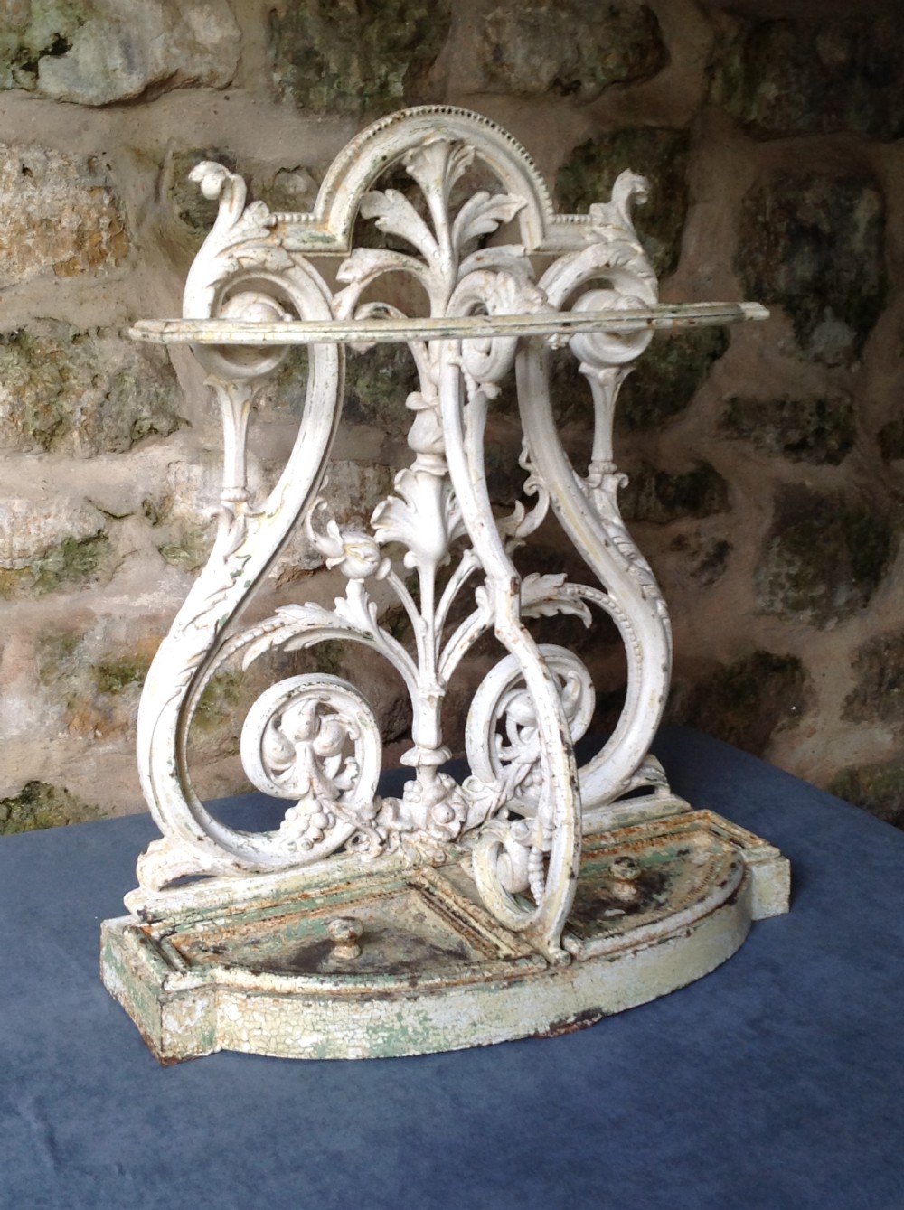An ornate off-white painted Victorian cast iron umbrella stand with botanical scrollwork and a twin drip tray base.