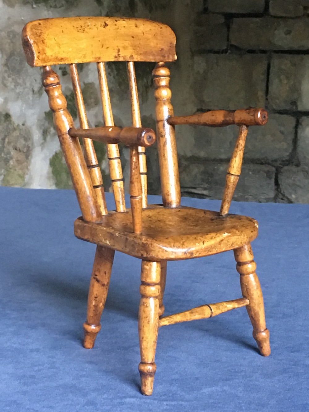 A wooden miniature Windsor armchair featuring turned spindle back supports, curved armrests, and turned legs.