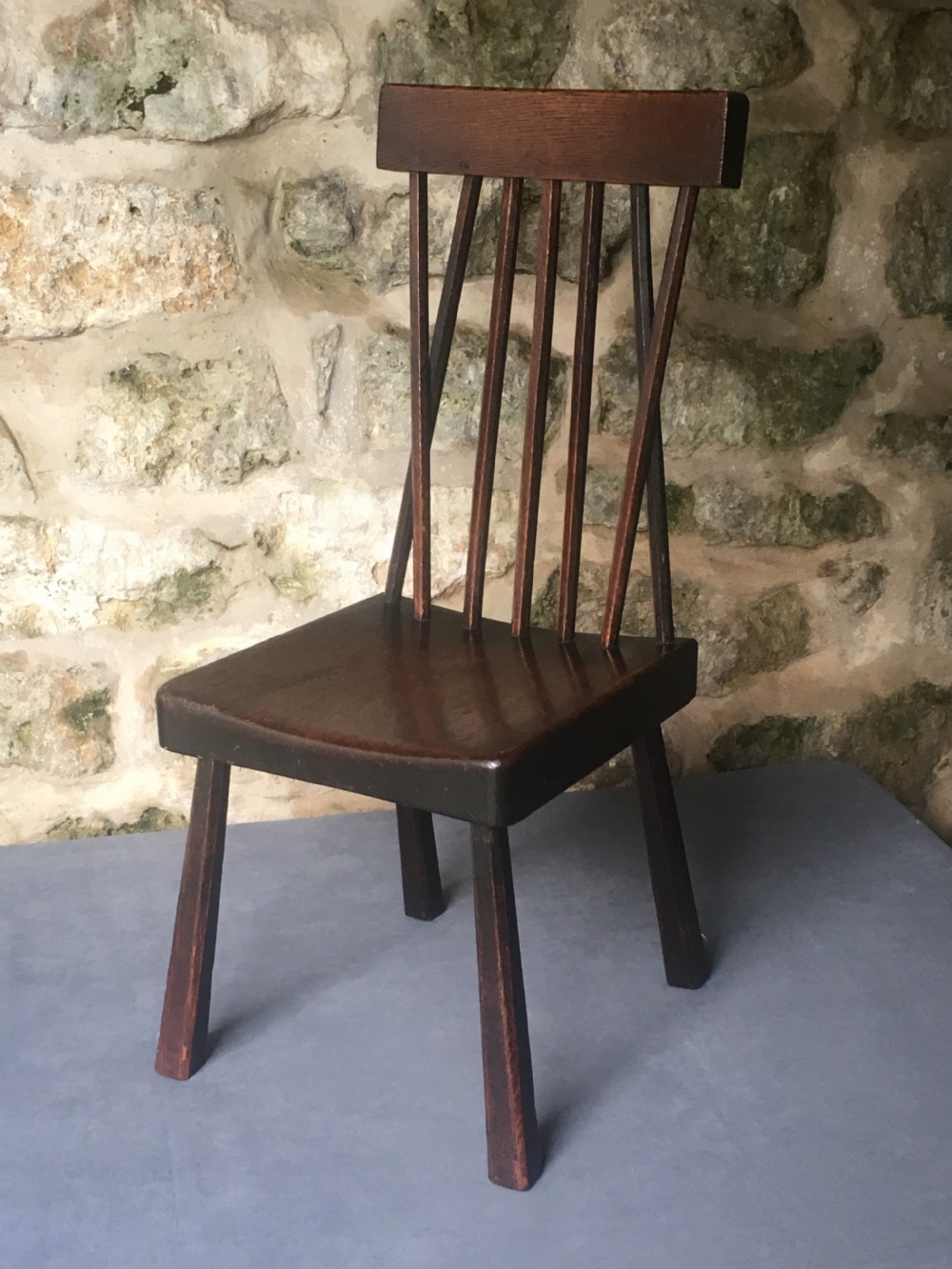 A dark oak side chair featuring a spindle back rest, solid wooden seat, and tapered splayed legs.